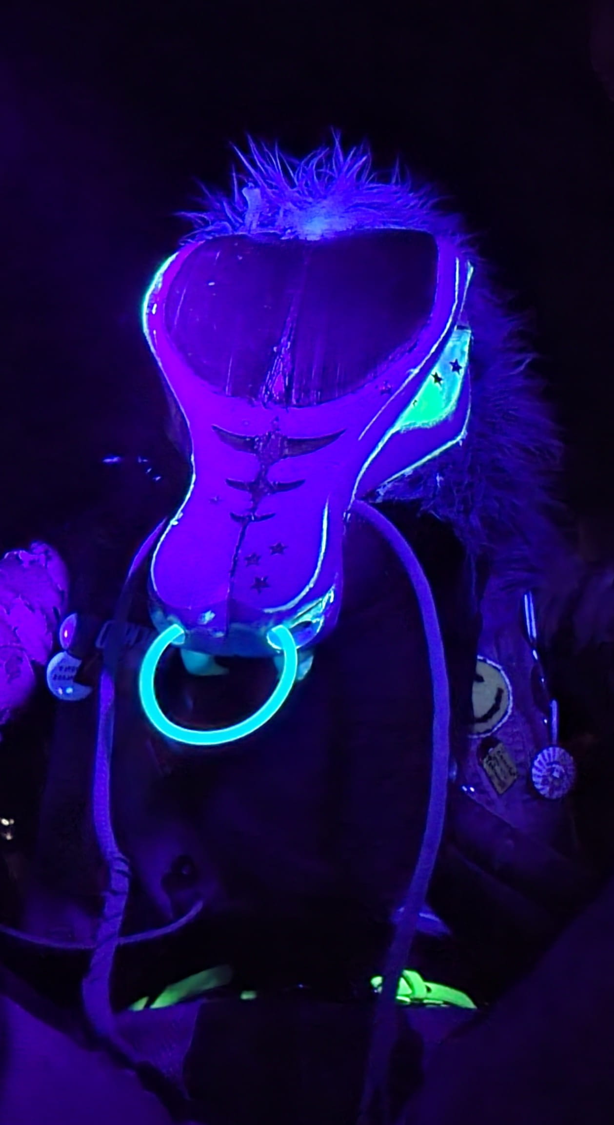 A blacklight image of the weevil fursuit, showing the patterning on the head and a glowstick nose ring