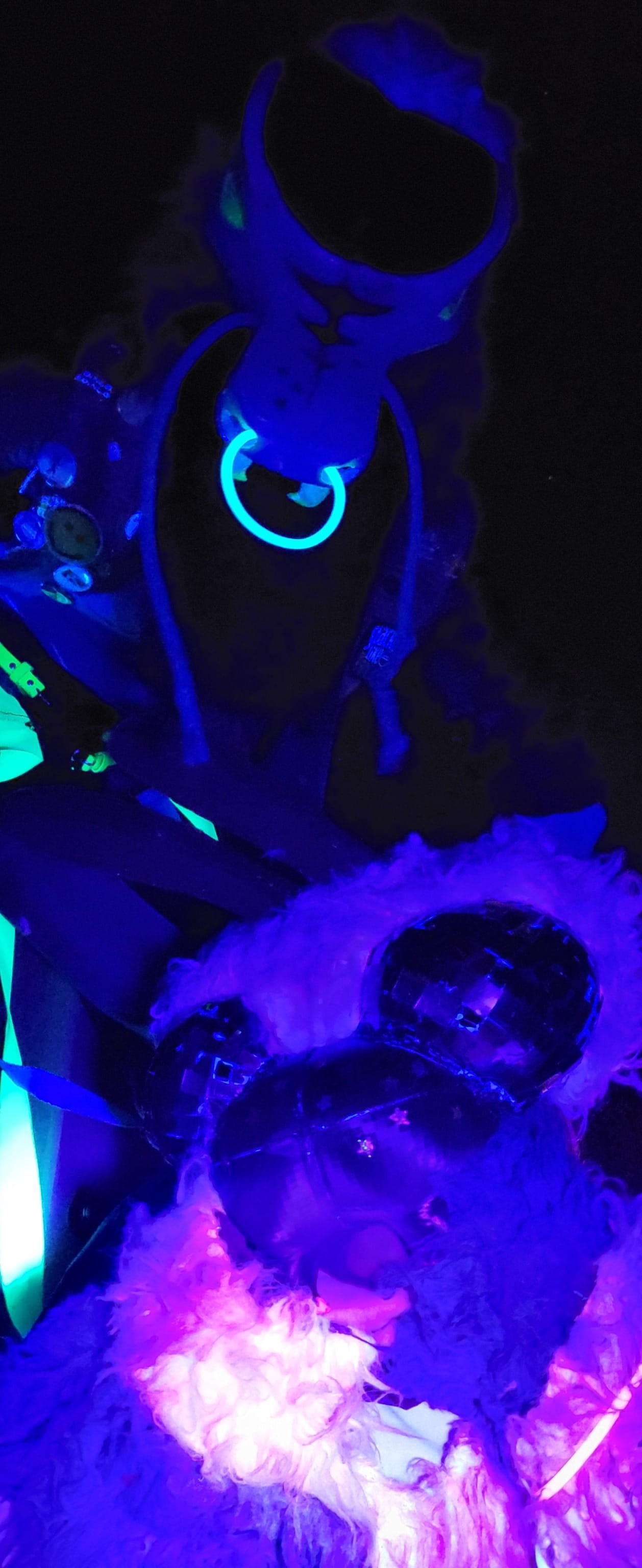 A blacklight photo of two fursuiters, one a blue weevil and the other a pink velvet ant