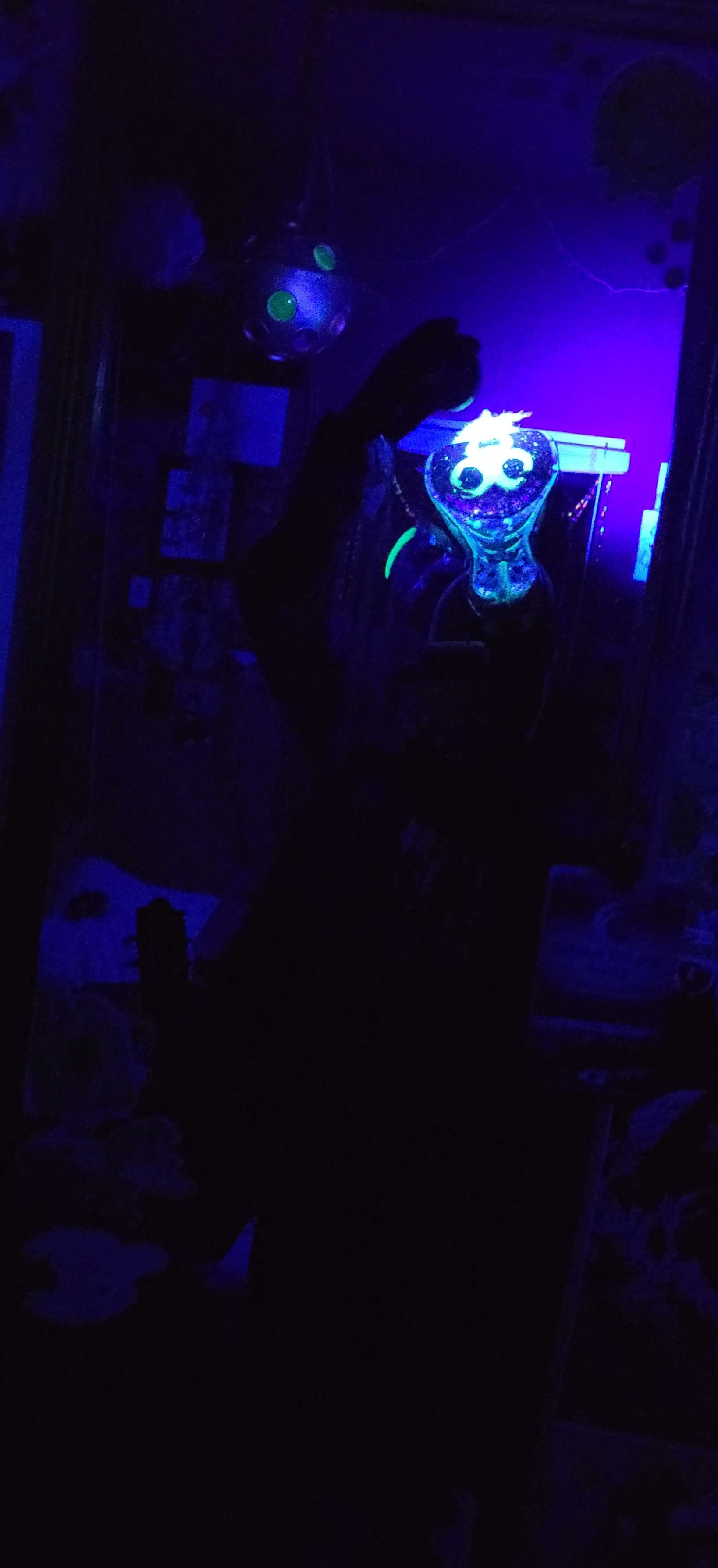 A blacklight mirror selfie of the weevil, showing a flourescent biohazard sign on the head