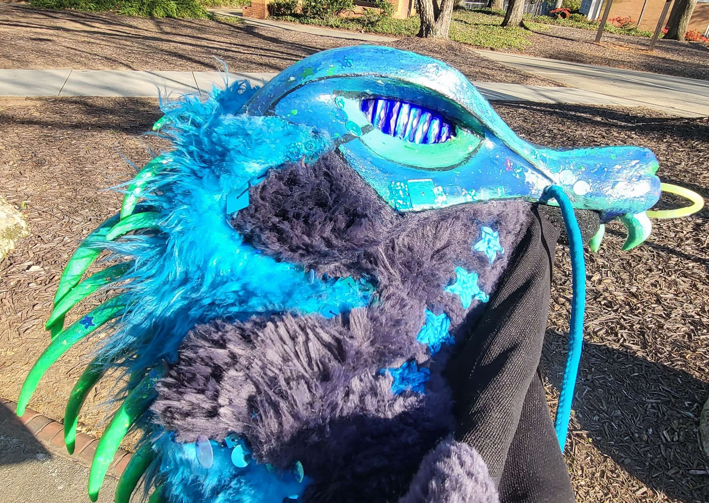 A side image of the weevil head, showing off the blue and black fur patterning along the next, blue star embroidery, and green spikes along the back.